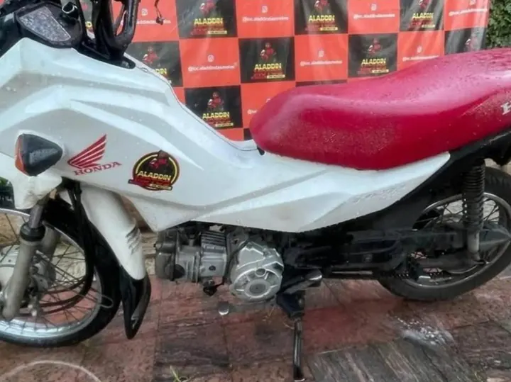 Honda Pop 110i branca com banco vermelho em frente ao painel da Aladdin Motos