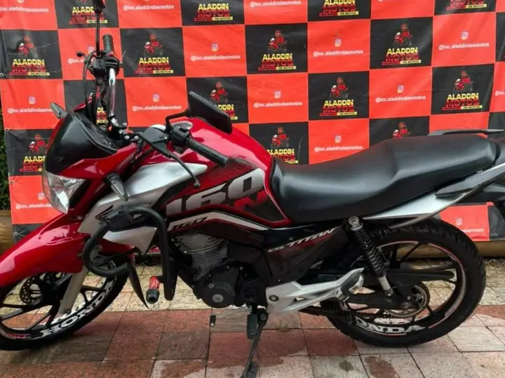 Honda CG 160 Titan vermelha em frente ao painel da Aladdin Motos